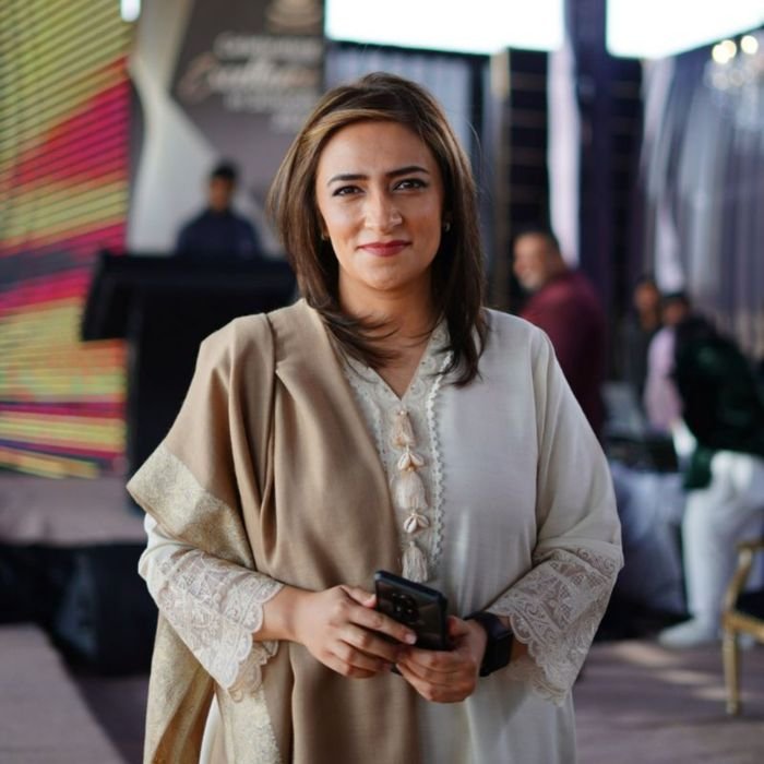 Elegant businesswoman holding smartphone, smiling at an event in Dubai. Professional attire and warm ambiance.
