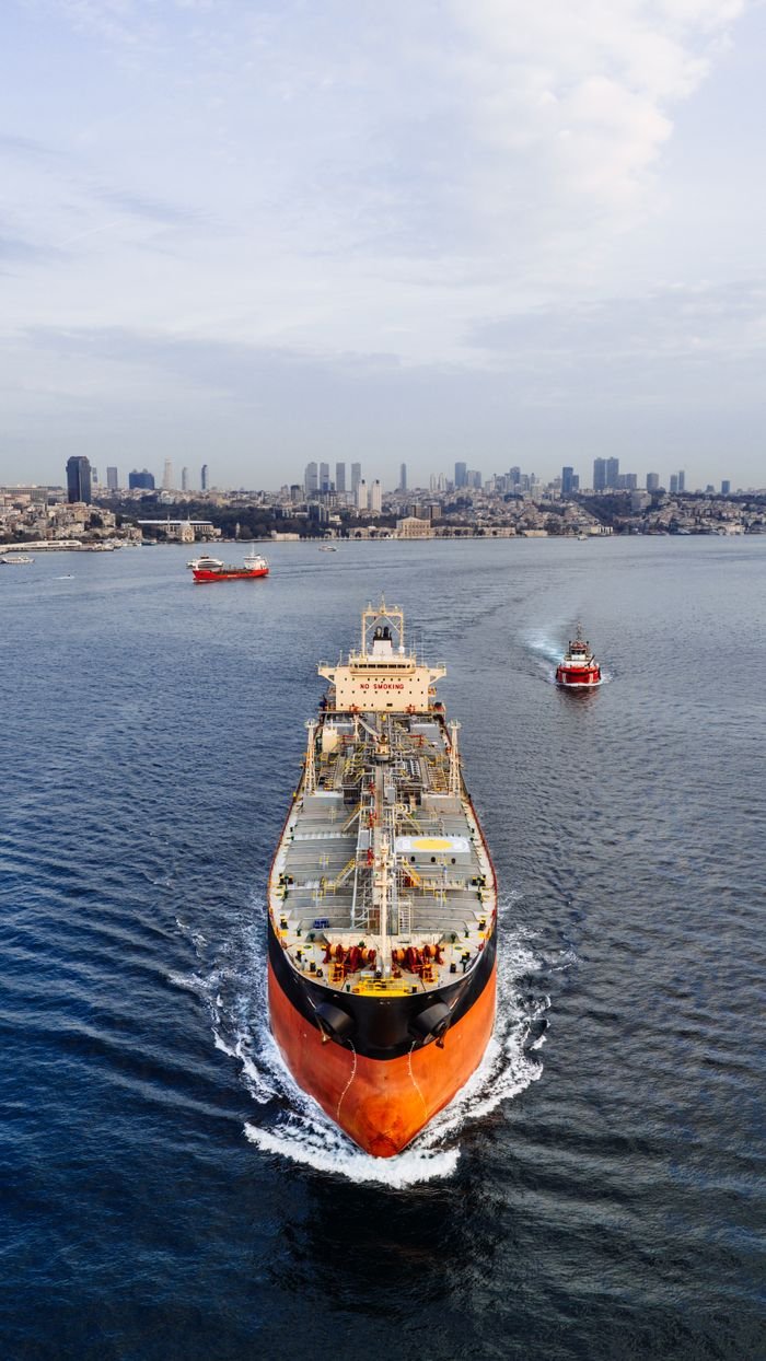 Aerial shot of a cargo ship navigating through Istanbul with the city skyline in the background.