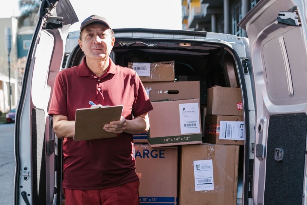 Delivery person with a clipboard beside a van loaded with boxes