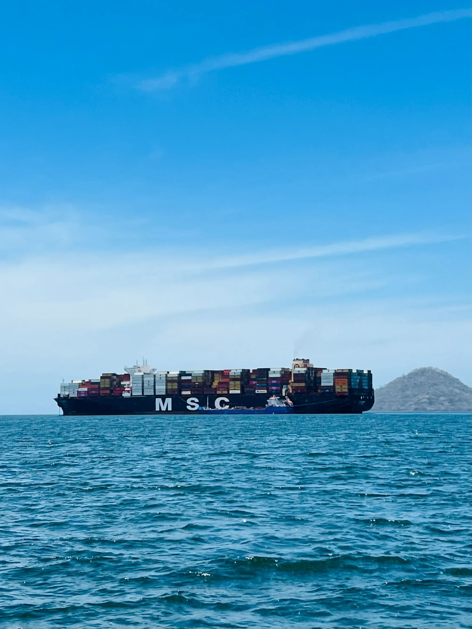 Cargo ship carrying containers on a calm ocean under a clear blue sky