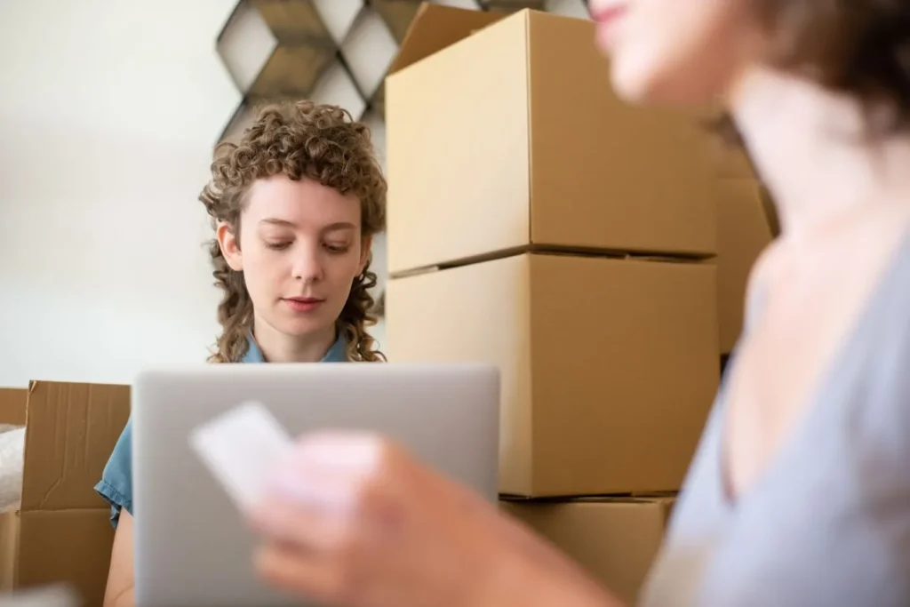 Business owner packing boxes and checking orders on a laptop